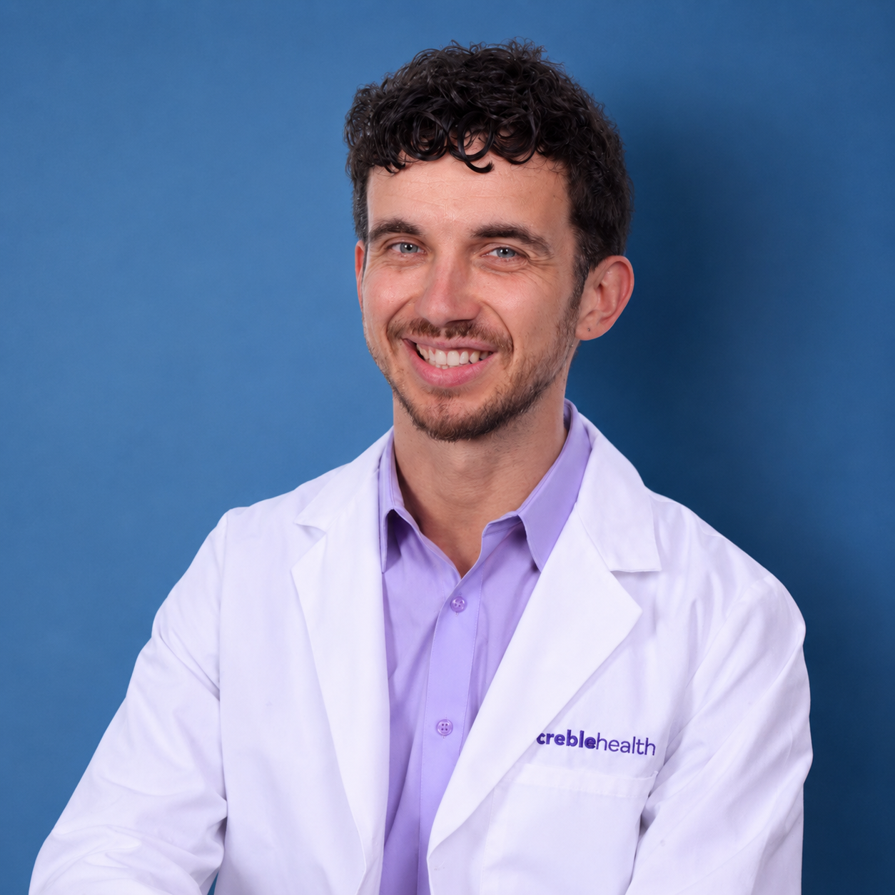 Studio portrait of Dr. Ben Thompson in a white coat on a blue background